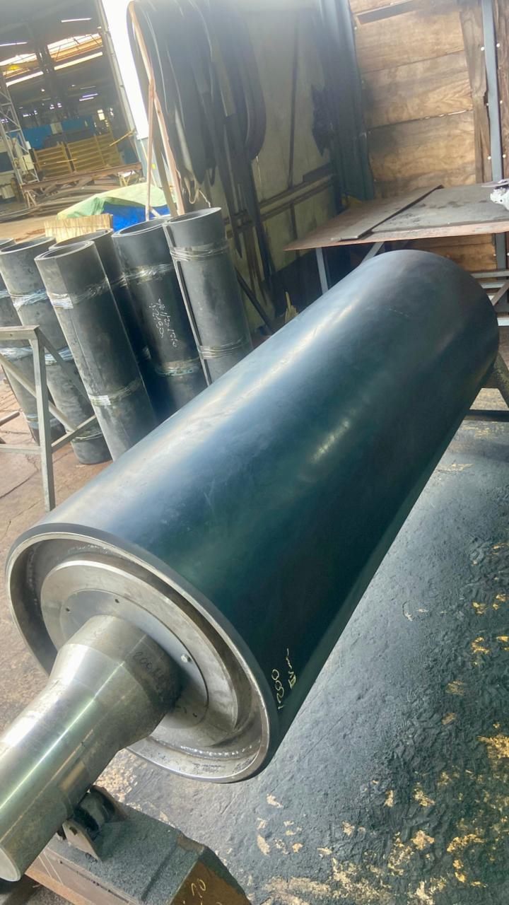 Rolo de grande porte com revestimento de borracha liso, na oficina, com outros rolos ao fundo