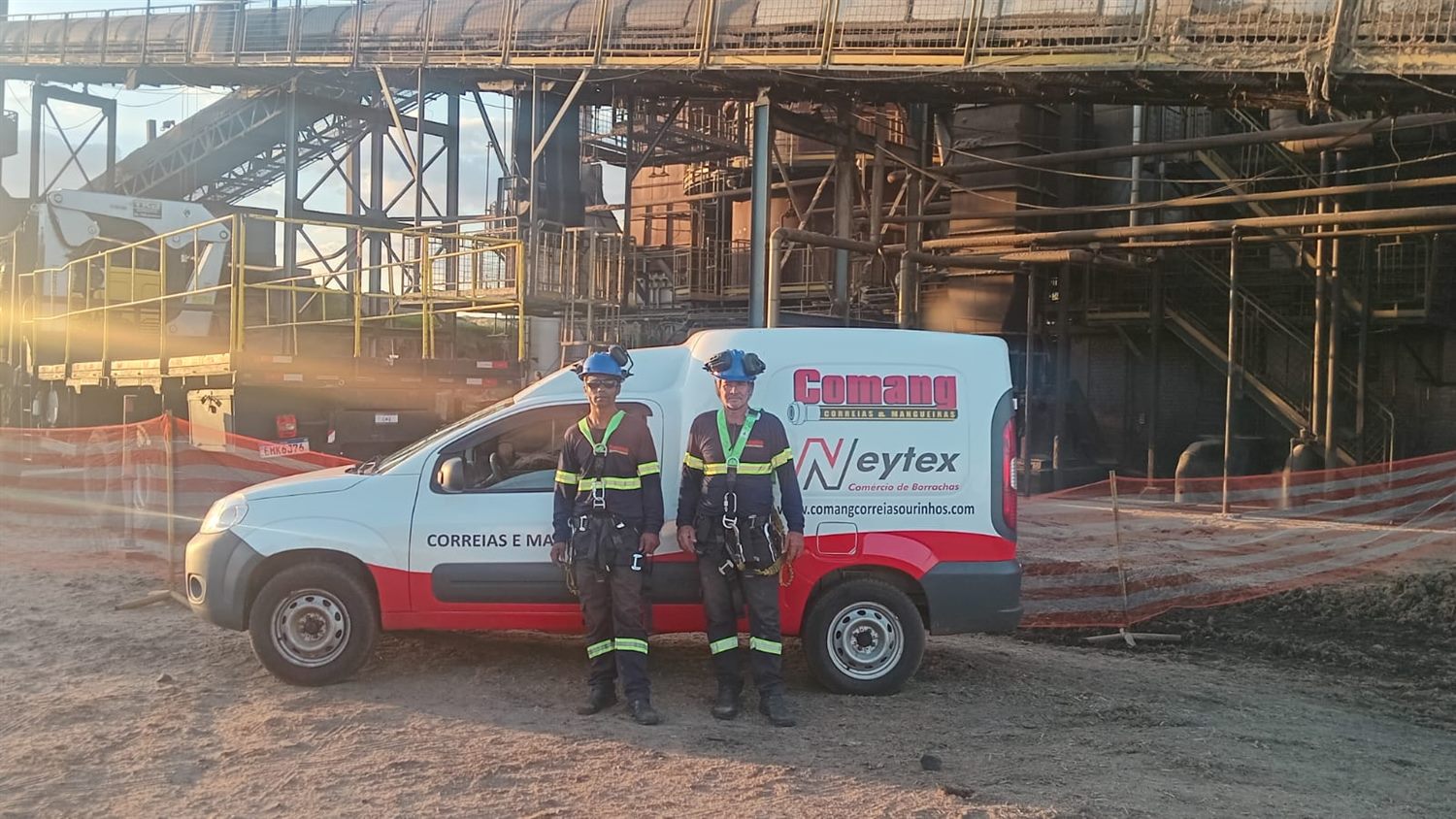 Equipe técnica da Comang, de capacete e cinto de segurança, em frente ao veículo da empresa dentro de uma planta industrial